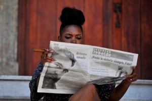 A woman smokes a cigar as she reads the newspaper