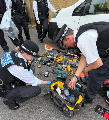 Met police officers crouch over a pile of power tools on the pavement