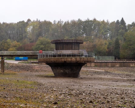 A large metal funnel-shaped structure stands on the drained bed of Ardingly reservoir
