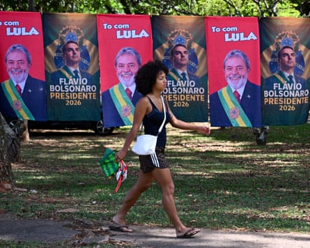 A woman walks past flags and towels bearing the images of Brazil’s president and presidential candidate, Luiz Inácio Lula da Silva, and rightwing senator and presidential candidate Flávio Bolsonaro in Brasilia