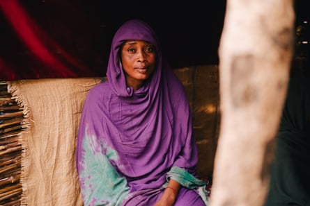 A young woman in a purple shawl sits in a hut