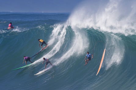 Four surfers on the north shore of Oahu, Hawaii, on a huge wave, with one surfer having lost contact with his board