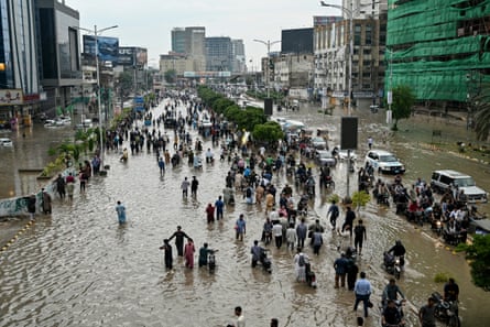 People wade and push motorcycles along a wide flooded city street