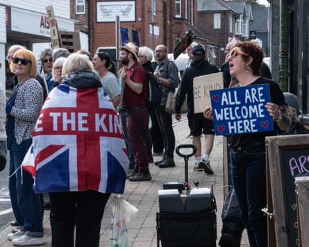 A woman wearing a union flag with the words “unite the kingdom” walks past a women holding a sign reading “all are welcome here”