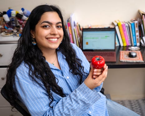 A women with a blue shirt smiles while holding a small kitchen timer shaped like a tomato