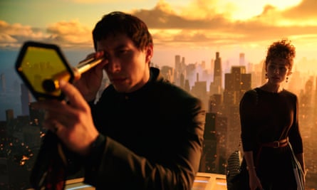 Man looks through a telescope with a screen, while a woman looks on. In the background is a high-rise city at sunset.