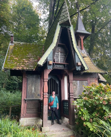 Rachel Dixon in front of a small old building with a steep roof, in a wood