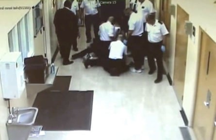 Screengrab showing prison guards crowding around a person (mostly obscured) on the ground