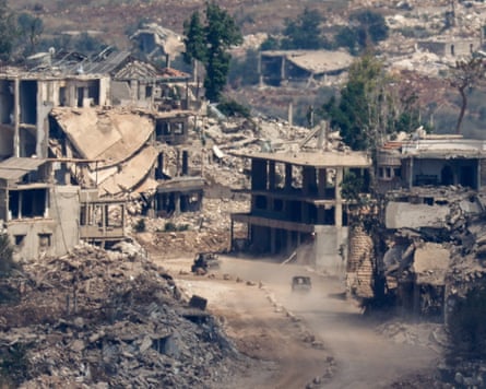 Israeli military vehicles drive past destroyed buildings