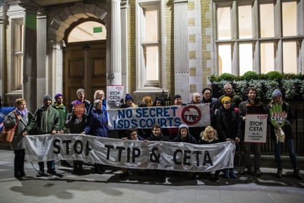 People stand outside a building holding banners that read ‘Stop TTIP and CETA’ and ‘No Secret ISDS Courts’.