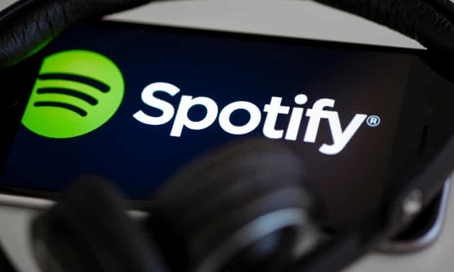 The logo of the music streaming service Spotify is displayed on a smartphone, with headphones lying on it