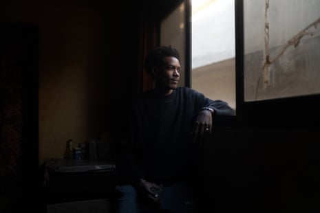 African man Nadir sits looking out a window. No view to be seen.