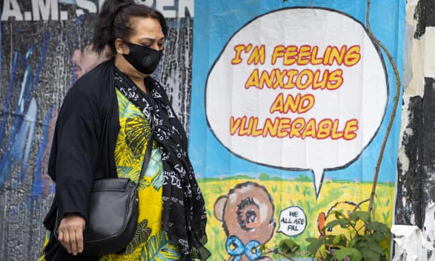 A woman wearing a face mask walks past a poster stating ‘I’m feeling anxious and vulnerable’ in east London.