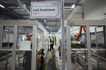Workers in hi-vis vests and hard hats stand next to enclosures where robotic arms are positioned