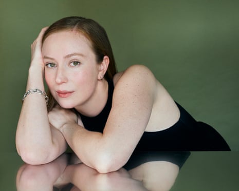 Hannah Einbinder in a black tank top leans on a reflective surface with her hand to her head