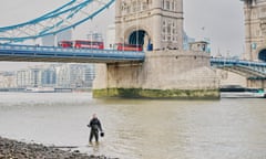A man stands in the Thames by Tower bridge, he is holding a bucket