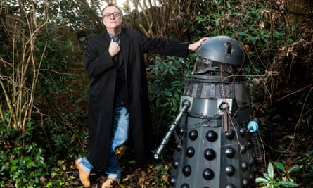 Russell T Davies stands next to a life-size Dalek in his garden