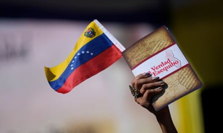 Uma mulher segura uma bandeira venezuelana e um livro sobre a disputa territorial de Essequibo.