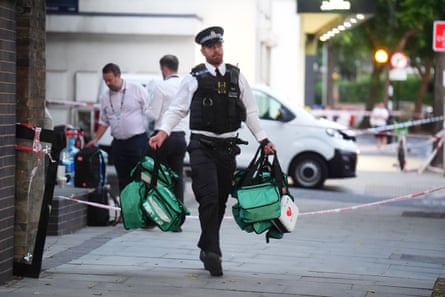 A uniformed, male police officer carries green medical equipment away from the crime scene.