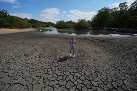 A worker from Hollow Ponds row boat hire stands in the exposed, cracked, and dried mud bed of Hollow Pond, where the water levels have significantly dropped, in east London.