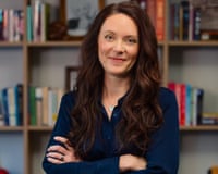 Carrie Joy Grimes in a navy blue shirt stands with arms crossed in front of a bookshelf
