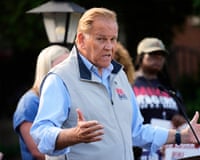 An older man gestures while speaking at a lectern.