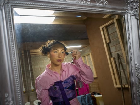 A young woman with her hair in bunches applies theatrical makeup in a mirror