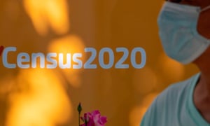 A person wearing a face mask walks past a sign encouraging people to complete the census in Los Angeles, California.