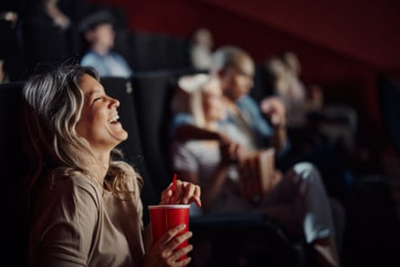 A woman laughs while watching a movie in a cinema.
