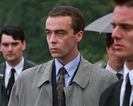 John Hannah in a coat in the rain in a funeral scene