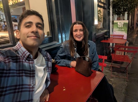 A selfie of Pardis in a check shirt and Alexandrea in denim jacket, sitting outdoors at a red table