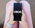Someone holding a mobile phone showing the Asos logo