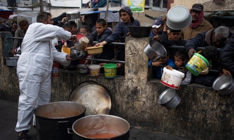 Palestinians, including many children, holding out pots as they queue for food aid