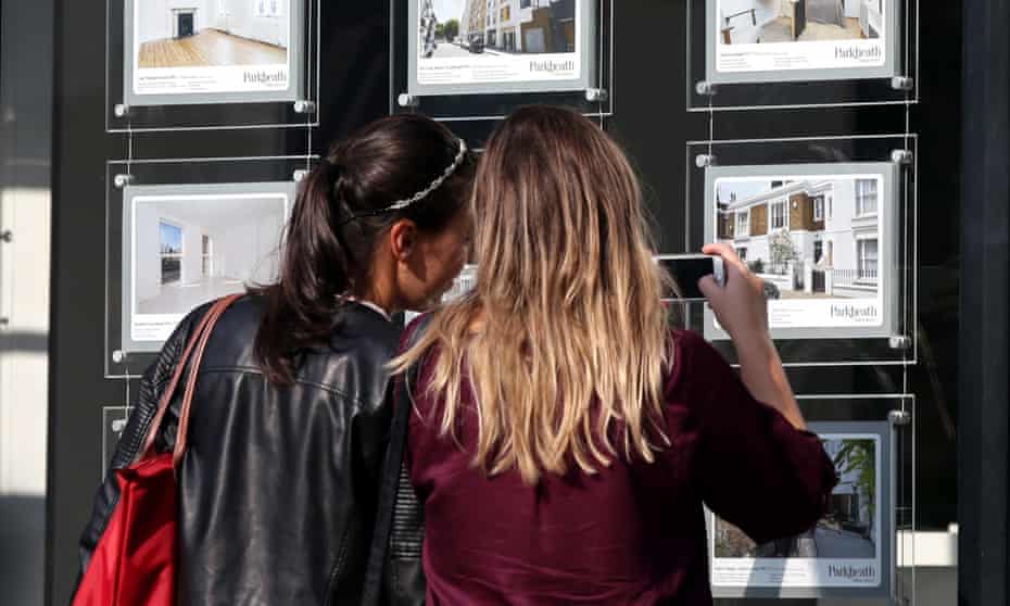 Two young women study an estate agent’s window in London. Record numbers of young Britons cannot afford to move out of their parents’ home.