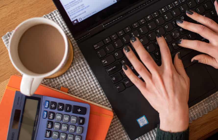 A woman using a laptop on a dining room table with a drink and a calculator