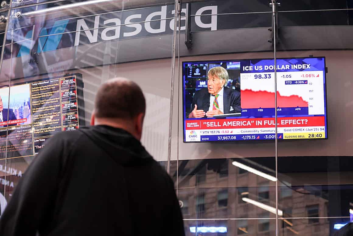 A man watches a screen showing CNBC near a Nasdaq sign