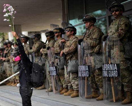 A demonstrator raises his hand holding flowers as members of the national guard stand outside a federal building in Los Angeles, California, on Saturday.