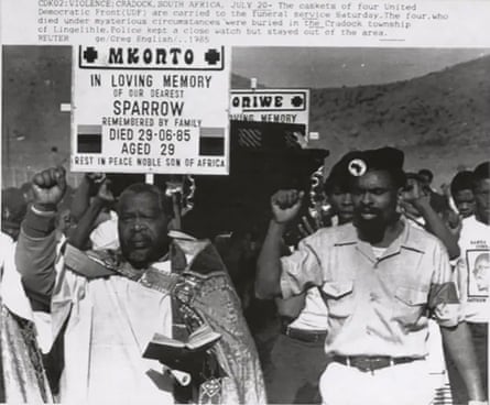 Black and white image of men with fists raised leading a funeral procession