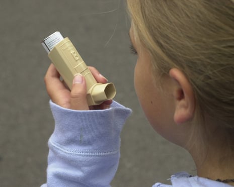A young girl holds an asthma inhaler to her mouth, preparing to use it