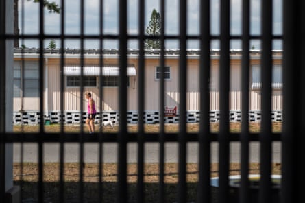 A woman walks past a for sale sign for a mobile home at Down Yonder mobile home park, seen through a fence.