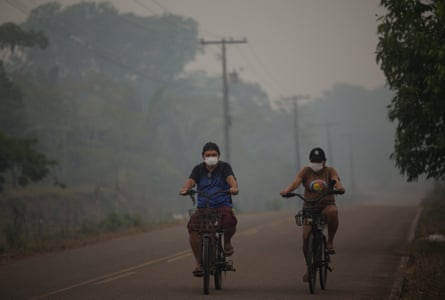 People wear masks while riding bicycles on a road shrouded in smoke from a wildfire in a deforested area of the Amazon rainforest in Autazes, Brazil, in October 2026.