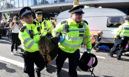 Police officers carry away an activist as Extinction Rebellion protesters block a road with caravan in central London