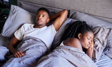 Young man looking unhappy while lying in bed with his sleeping partner.