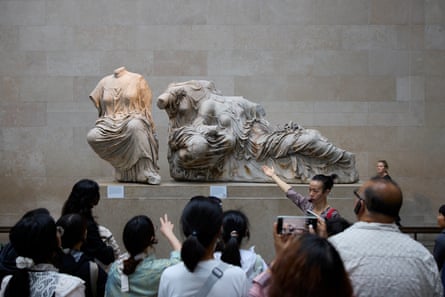 A tour group listens to their guide in front of a display of the Parthenon scupltures at the British Museum, London.