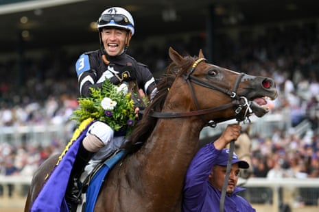 Jockey Juan Hernandez smiles while holding a winning garland atop his racehorse Bacio.