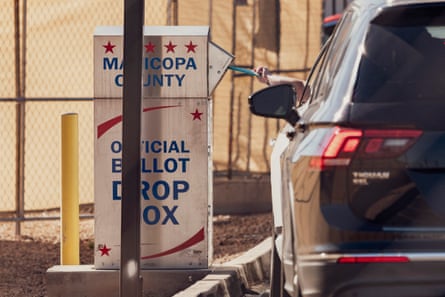 A person placing their ballot into voting box from their car