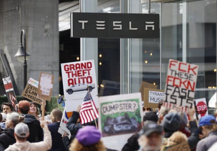 people hold up signs such as ‘grand theft auto’, ‘tyrant musk’ and ‘fck these fckn fascists’ while protesting outside tesla dealership