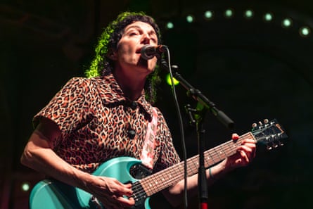 A woman wearing a leopard-print shirt plays a teal guitar and sings into a microphone
