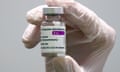 Gloved hand holds vial with AstraZeneca vaccine label