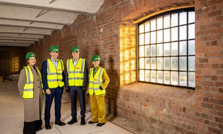 Helen Legg, Roland Rudd, Steve Rotheram and Maria Balshaw wearing hi-vis vest and green hard hats next to the original brick walls of Tate Liverpool